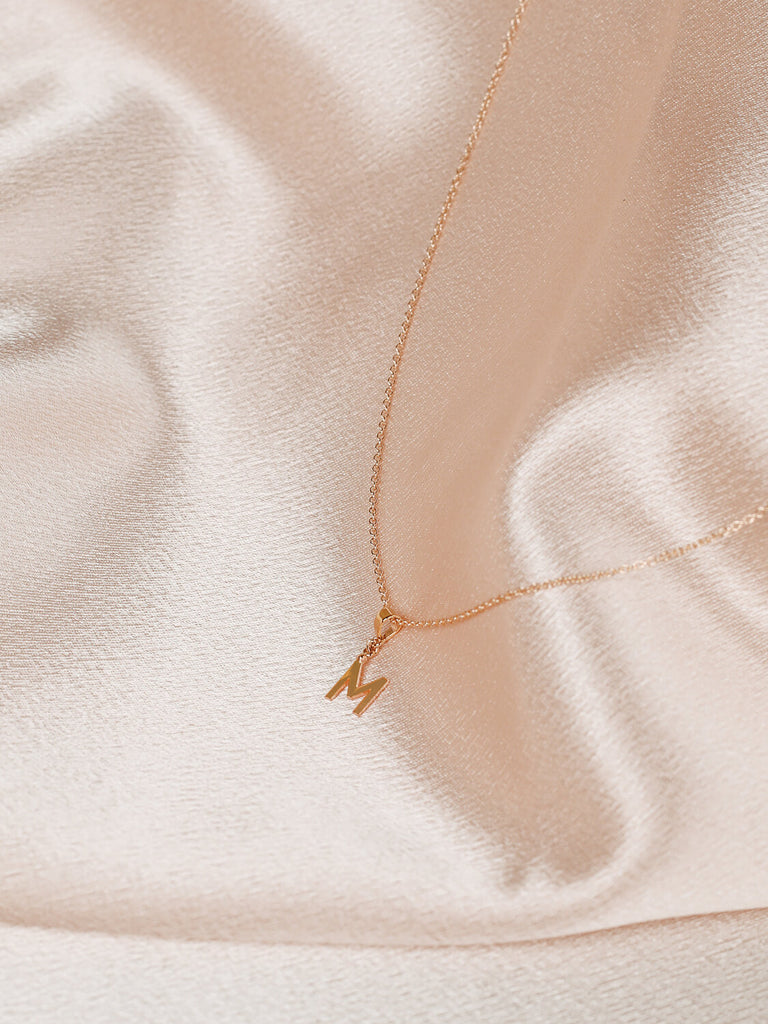 close up of m block monogram initial necklace in gold on satin