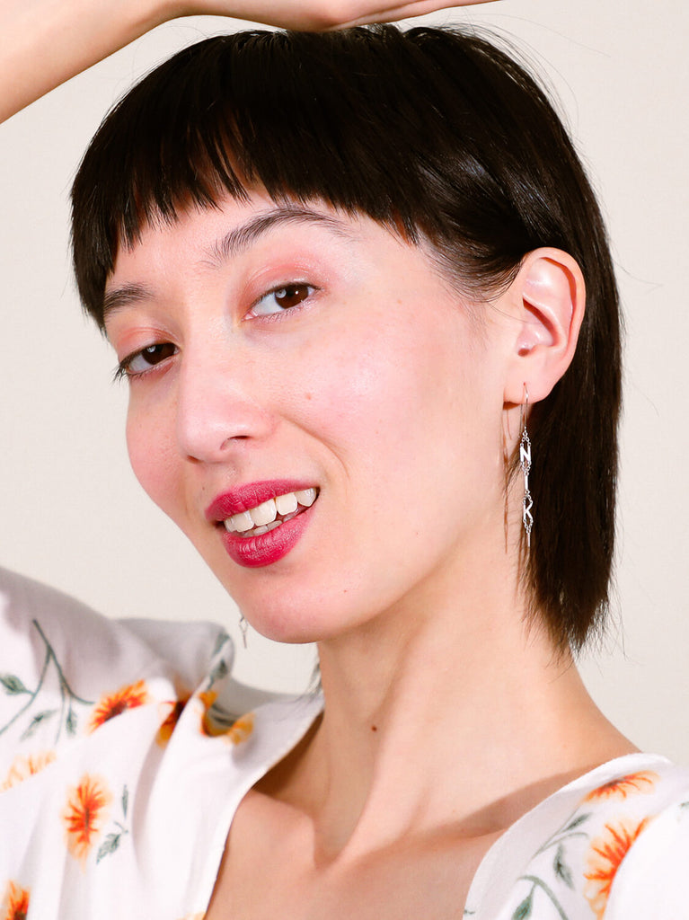 smiling female model wearing block name drop earrings in white gold