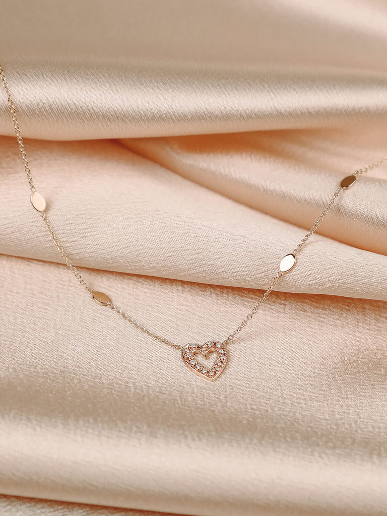 photo of charmed heart necklace in 14k rose gold with diamonds on pink satin background 
