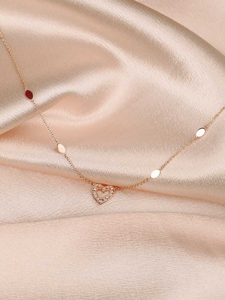 photo of charmed heart necklace in 14k rose gold with diamonds on pink satin background 