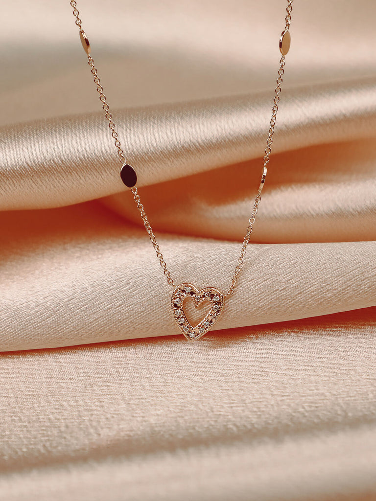 detail photo of charmed heart necklace in 14k rose gold with diamonds on pink satin background 