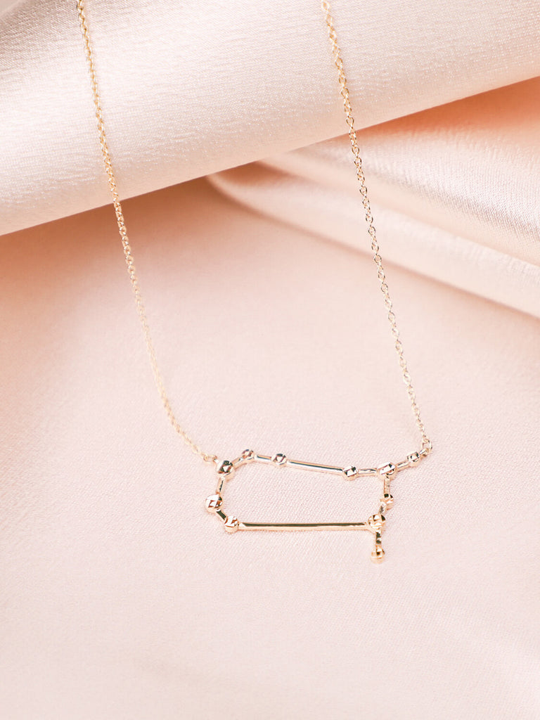 gold Gemini constellation necklace laying against satin