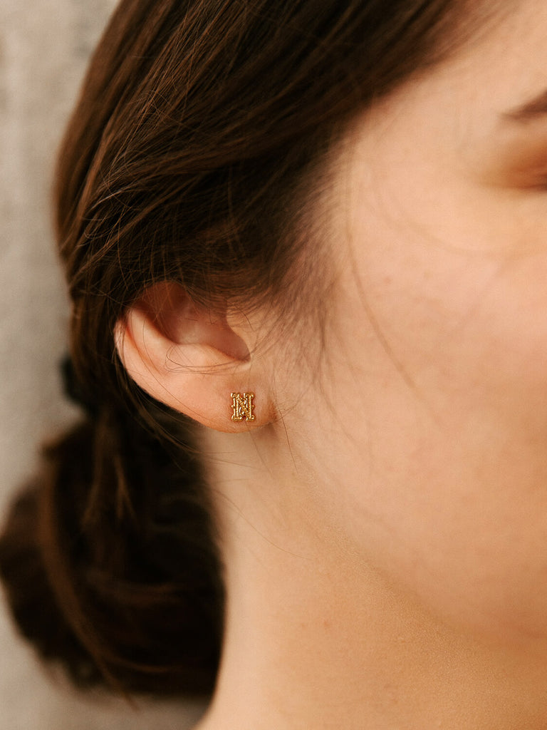 detail photo of gold gothic monogram post earrings on female model