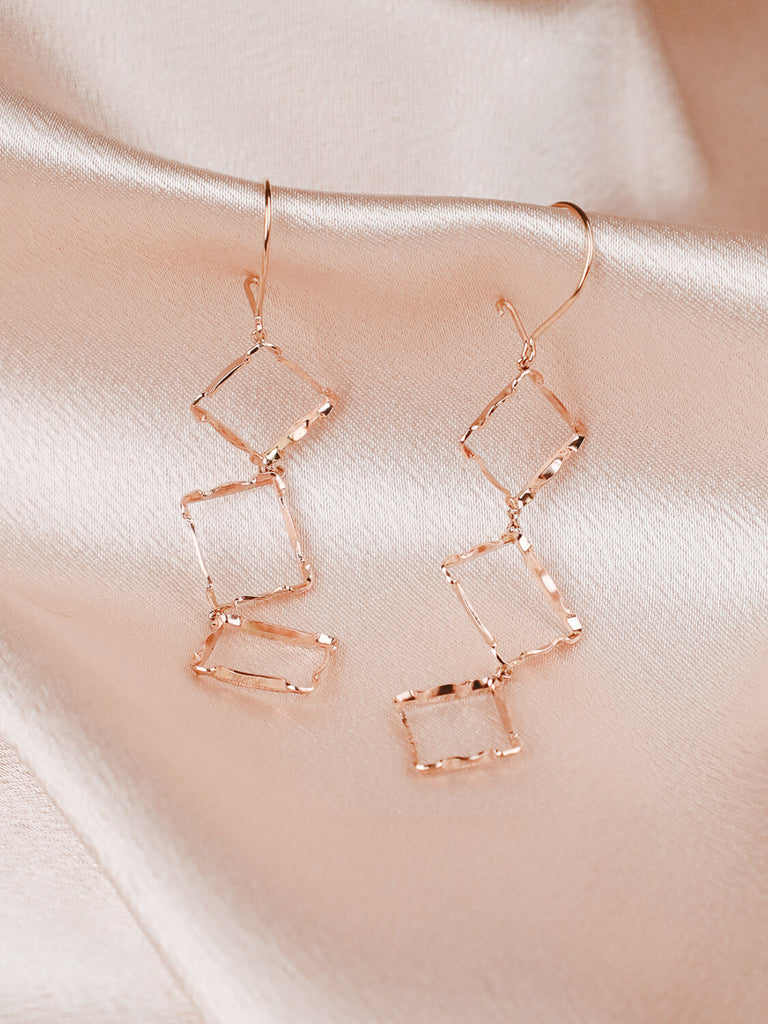 Close up of Halo rectangle stacked earrings on pink satin fabric