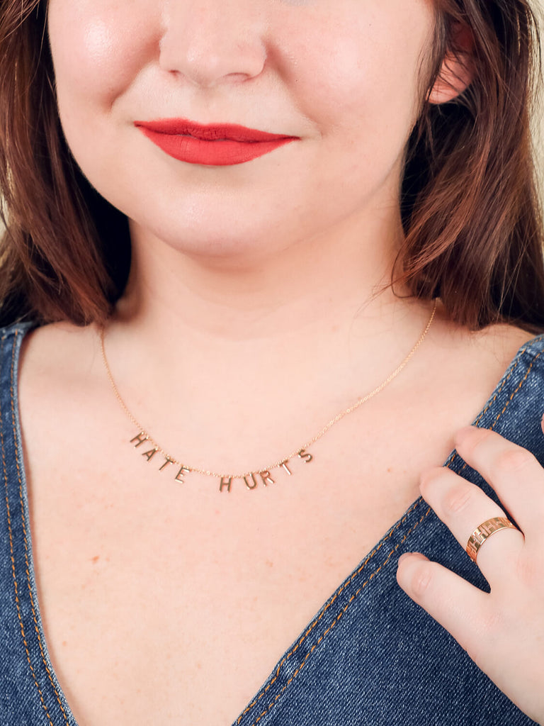 happy female model wearing "Hate Hurts" message necklace in yellow gold