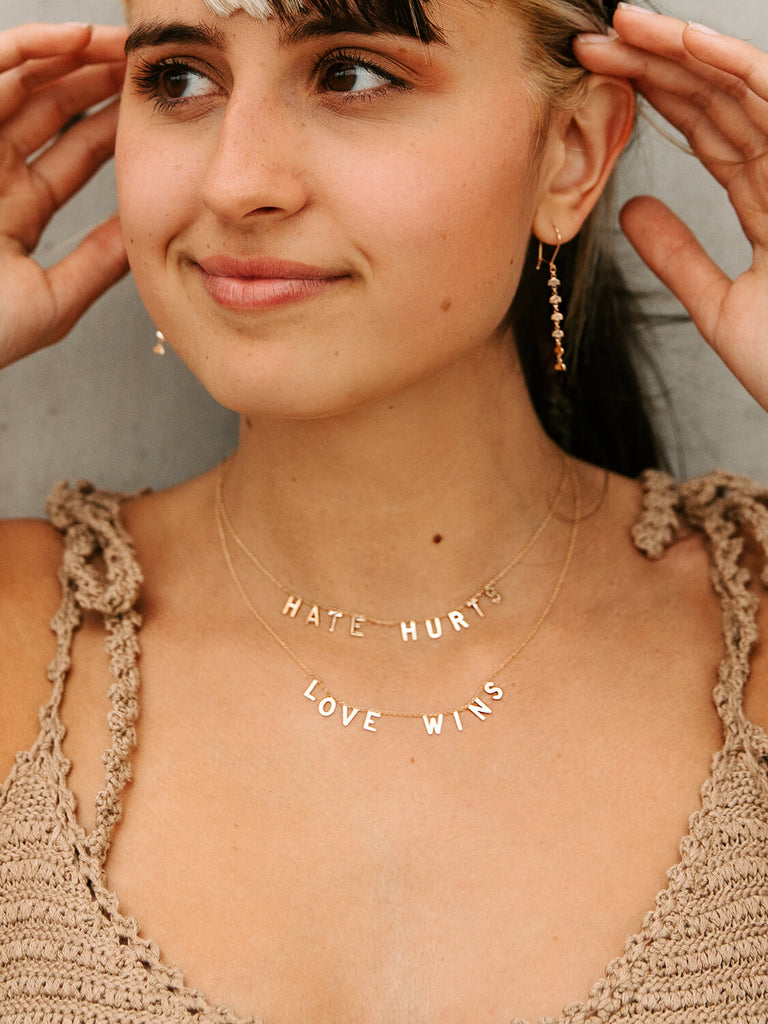 happy female model wearing "Hate Hurts" message necklace in yellow gold during golden hour
