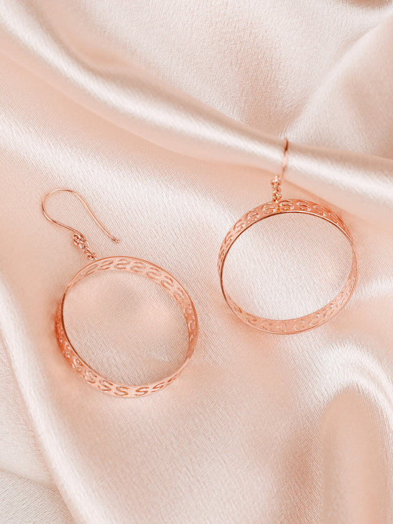 close up of "S" initial infinity hoop earrings in yellow gold on fabric background