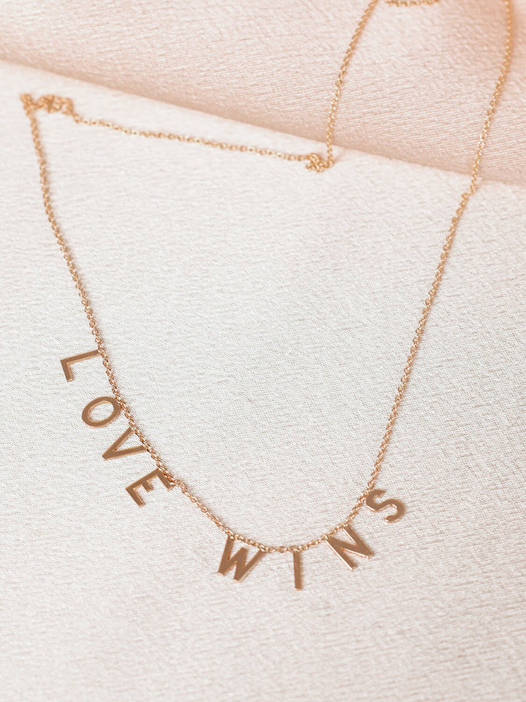 "Love Wins" message collection necklace in yellow gold on pink satin background