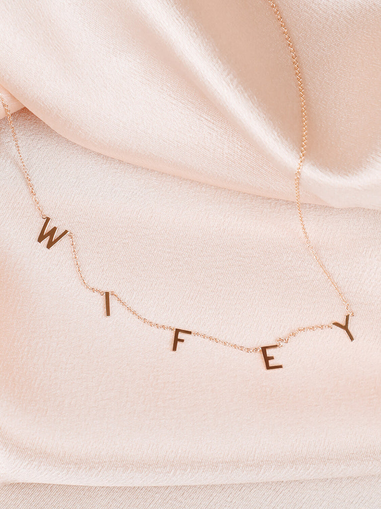"Wifey" message necklace in yellow gold on pink satin background