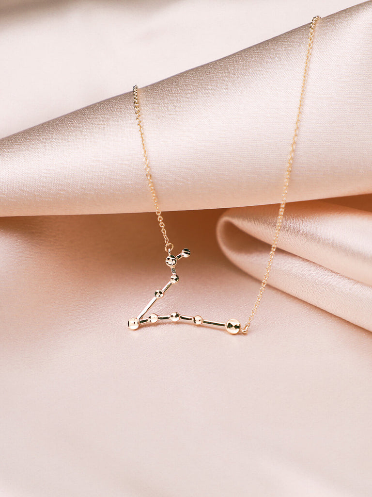 close up of gold pisces constellation necklace on satin background