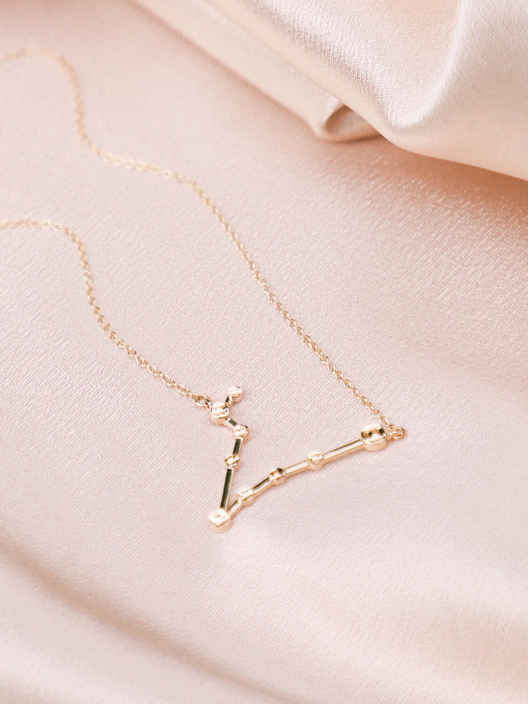  gold pisces constellation necklace laying down on satin background