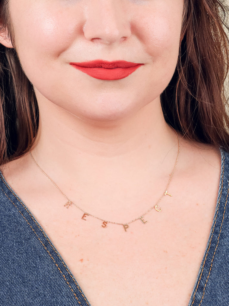 happy female model wearing yellow gold "Respect" message necklace  and bright red lipstick