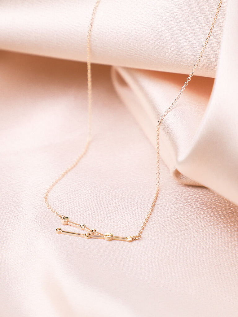 gold taurus constellation necklace laying down on satin background