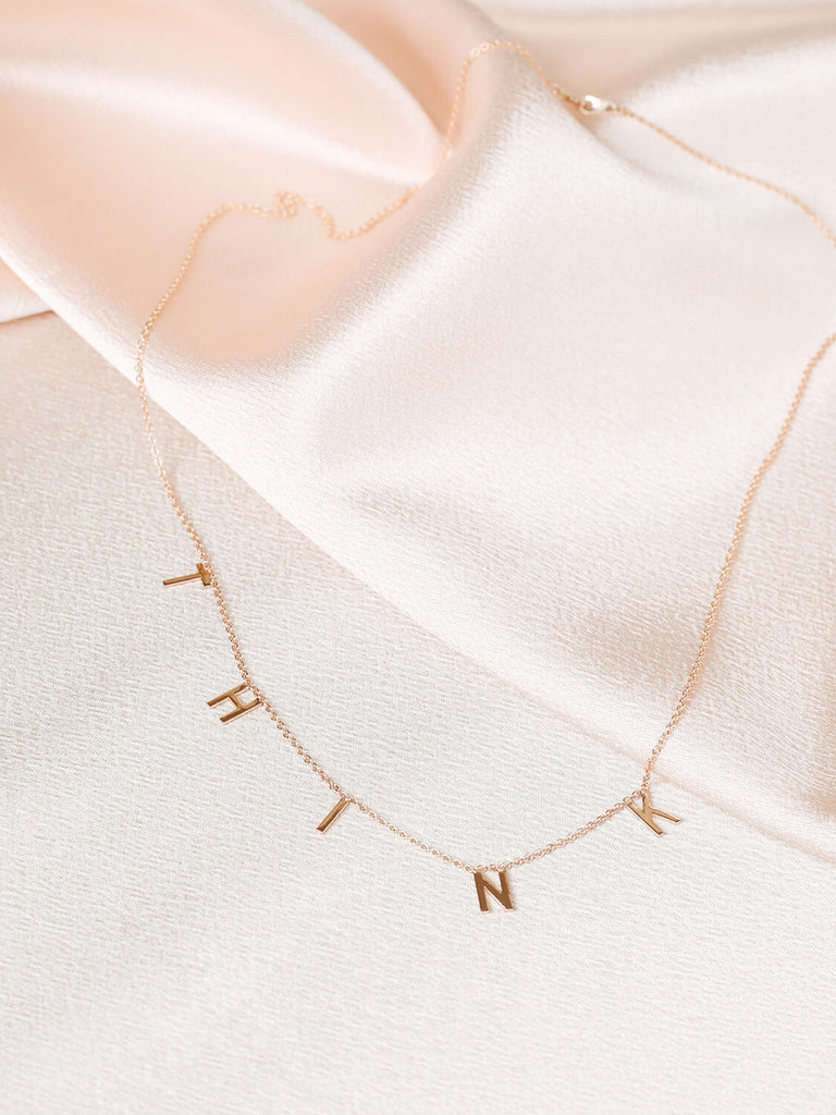 Close up of "Think" message collection necklace on pink satin
