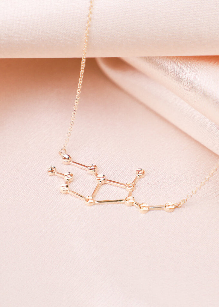close up of gold virgo constellation necklace on satin background