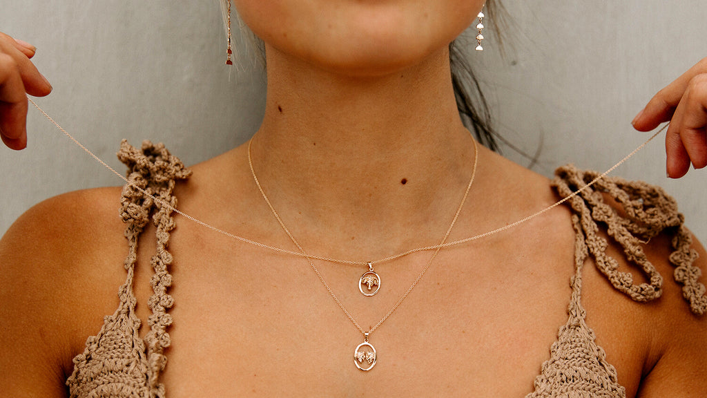 female model holing two zodiac charm necklaces on her tan skin