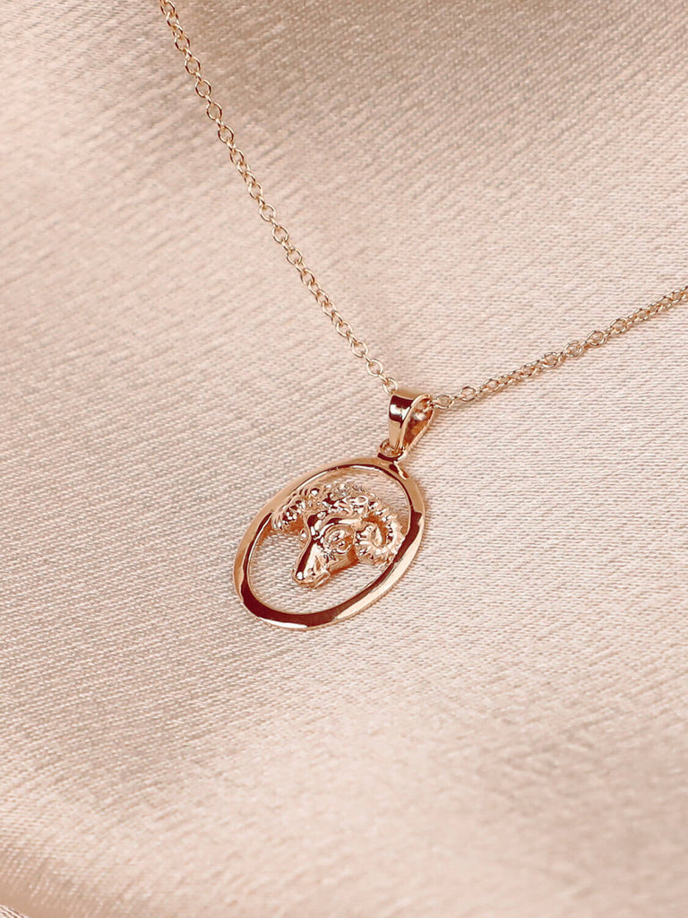 photo of aries yellow gold zodiac charm pendants necklaces on pink satin background