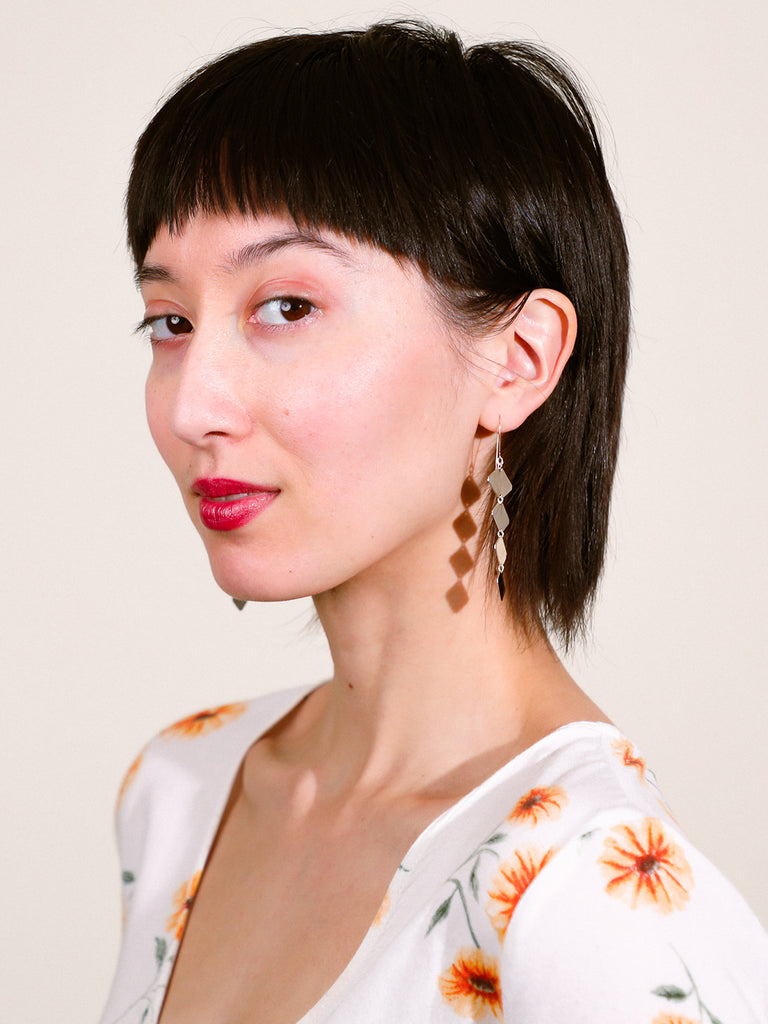 gold Artemis plate earrings on a model who is looking to the camera