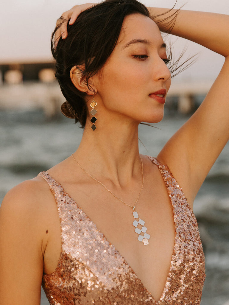 happy model wearing yellow gold Artemis plate necklace and earrings in sequin dress during golden hour