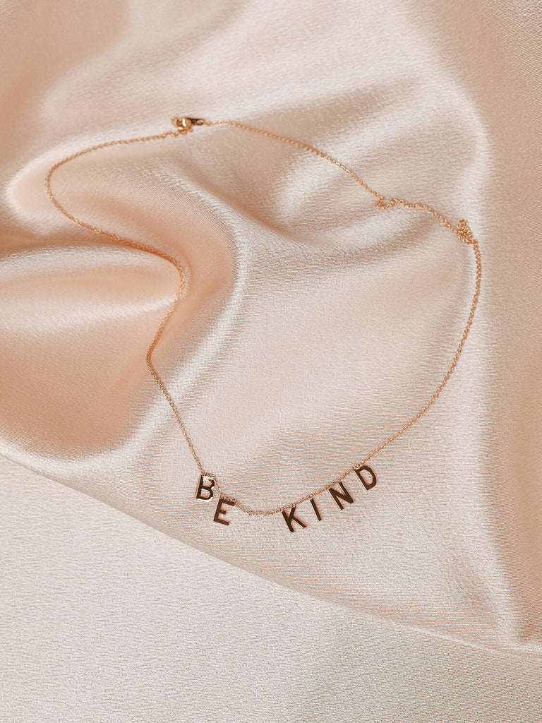arial view of gold Be Kind message necklace on pink satin