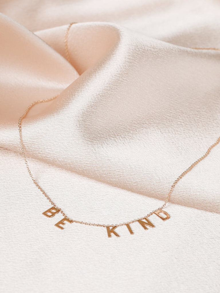 gold Be Kind message necklace on pink satin