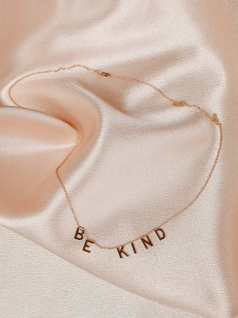 close up of gold Be Kind message necklace on pink satin