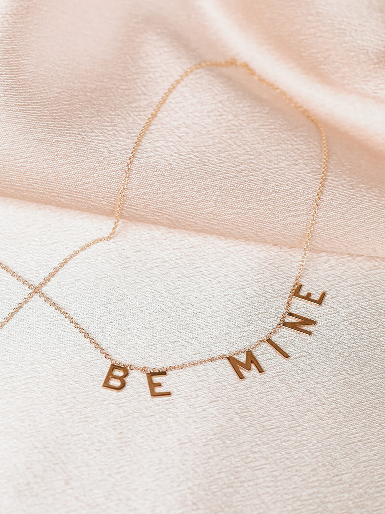 close up of gold Be Mine message necklace on pink satin