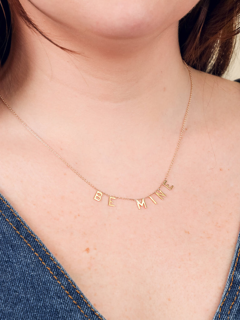 close up of gold Be Mine message necklace on smiling model
