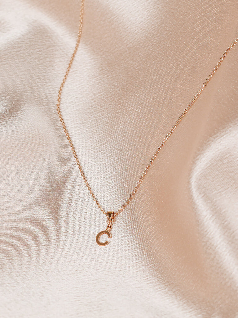 close up of c block monogram initial necklace in gold on satin