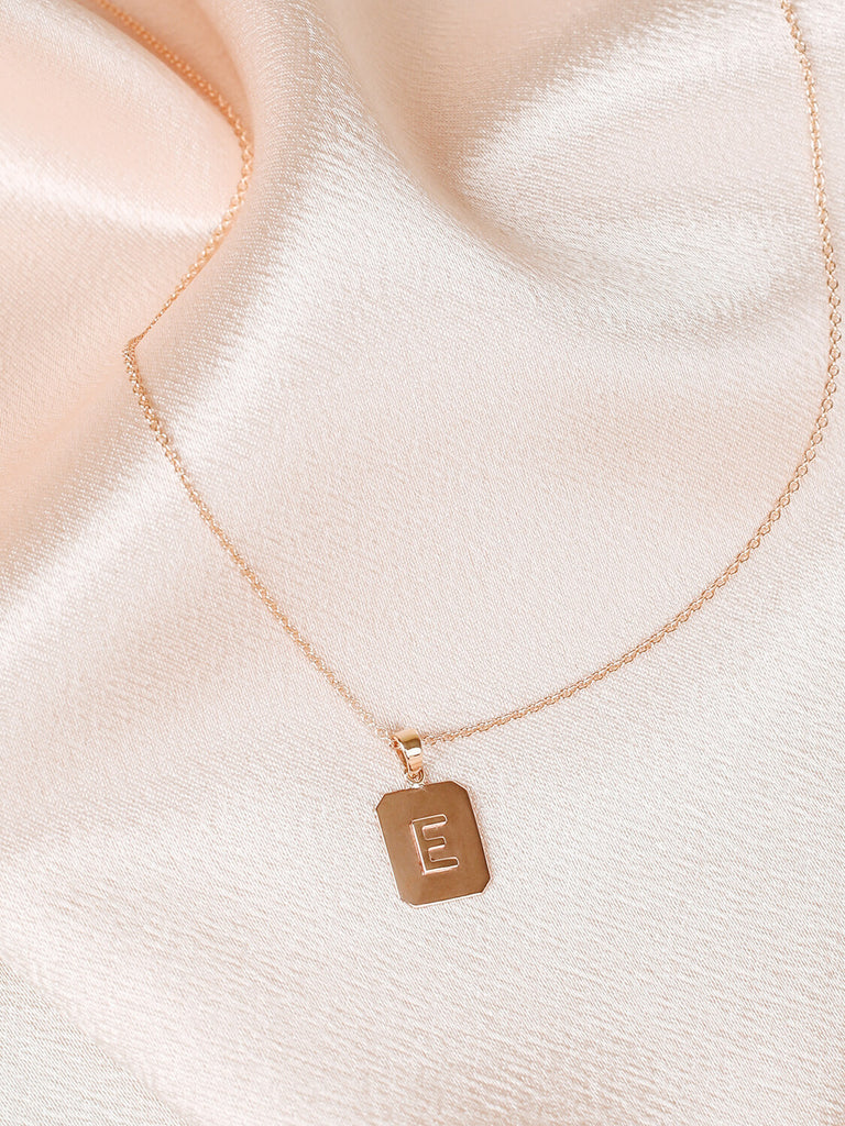 Close up of "E" Block Initial Necklace in yellow gold on pink satin background