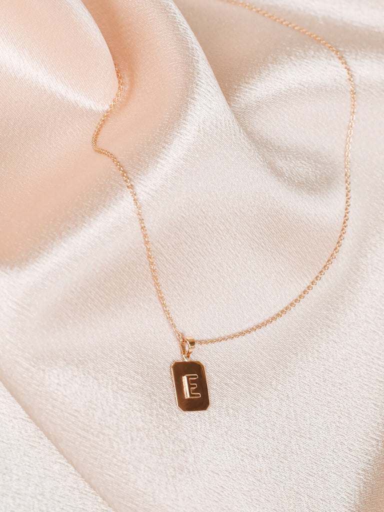 Close up of "E" Block Initial Necklace in yellow gold on pink satin background
