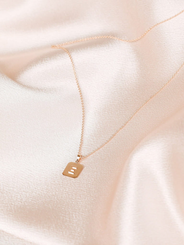 full view of "E" Block Initial Necklace in yellow gold on pink satin background