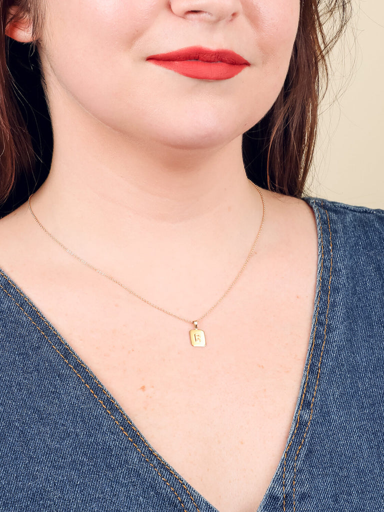 "R" block initial necklace in yellow gold on a happy female model