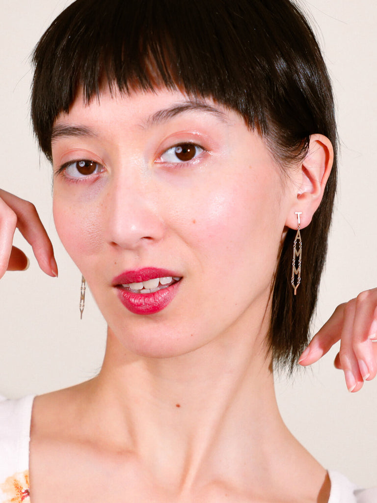 close up of female model wearing block name post drop earrings in white gold spelling Tammy