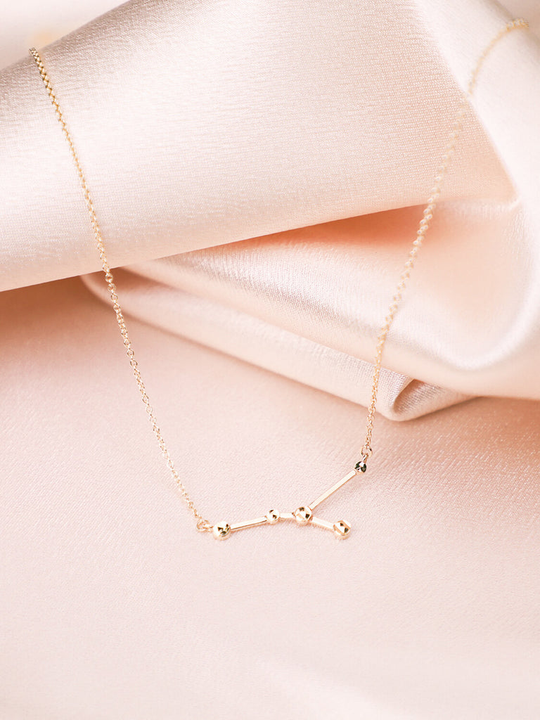 gold cancer constellation necklace close up on satin background