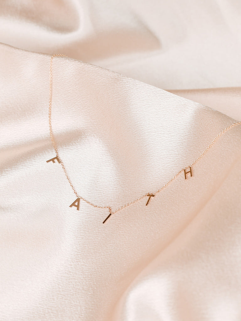 close up of Faith message necklace in yellow gold on pink satin
