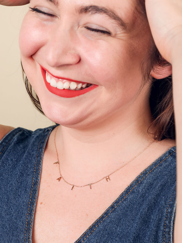 close up of laughing female model wearing Faith message necklace in yellow gold