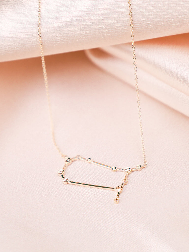 detail photo of gold Gemini constellation necklace against satin