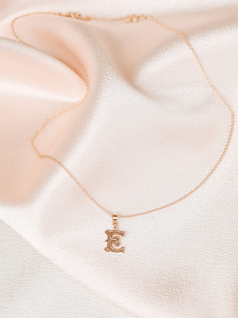 full view of "E" gothic initial necklace in yellow gold on pink satin