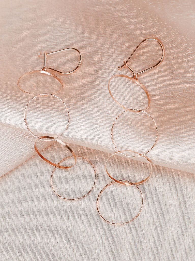 Close up of halo looped earrings in yellow gold on pink satin fabric background