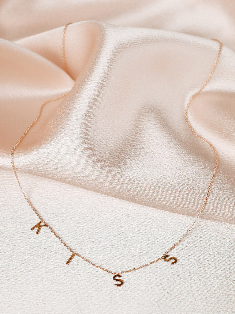 "Kiss" message collection necklace in yellow gold on pink satin background
