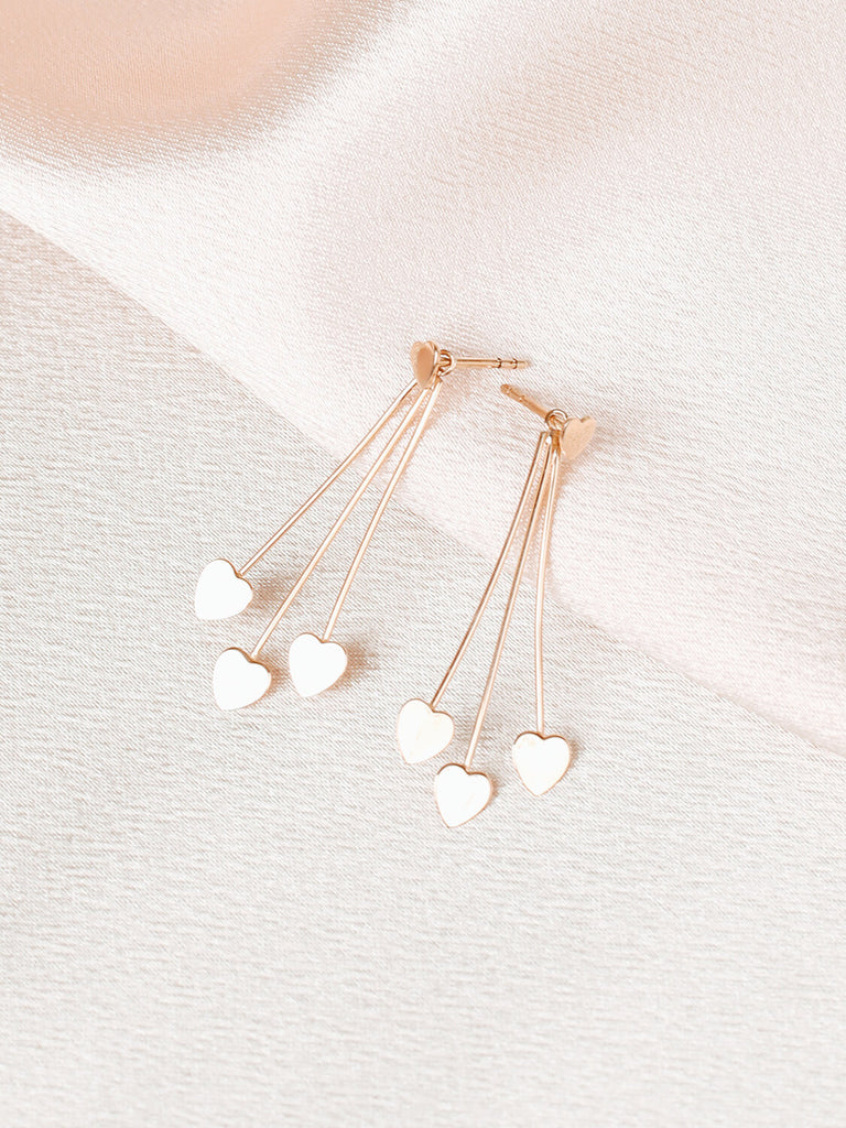 close up of four heart earrings in yellow gold on pink satin background 