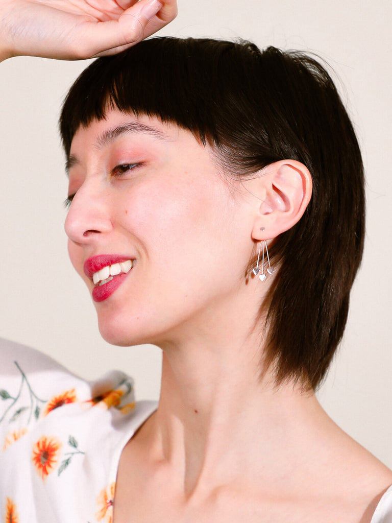 smiling female model wearing four heart earrings in yellow gold