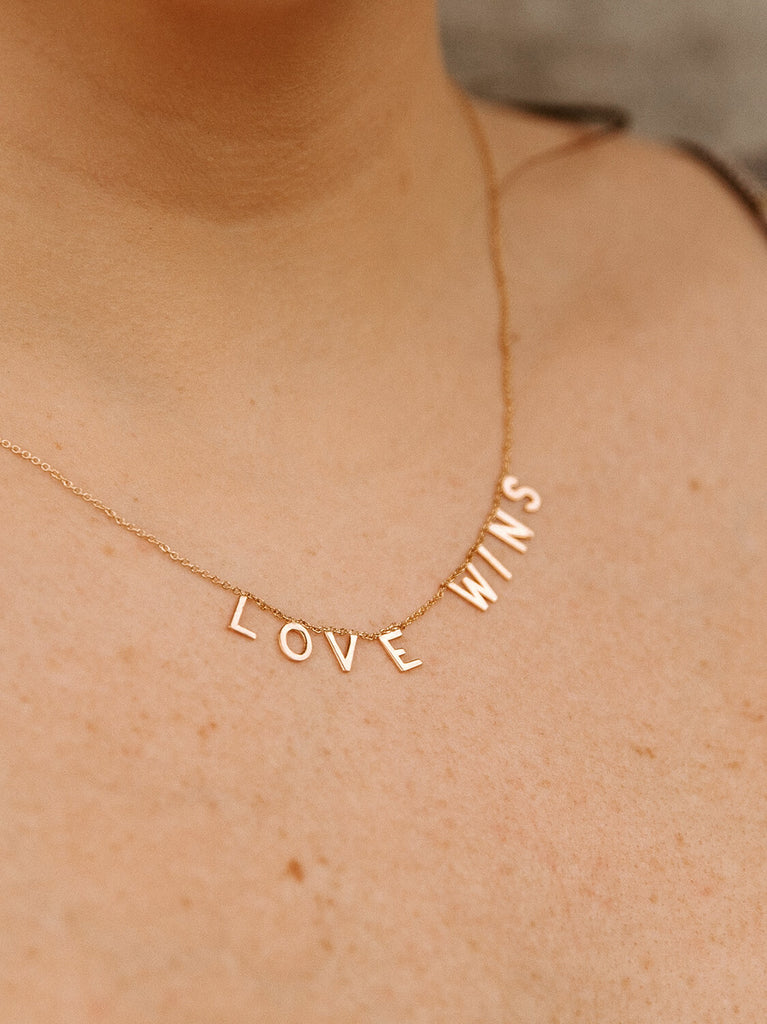 "Love Wins" message collection necklace in yellow gold on female model