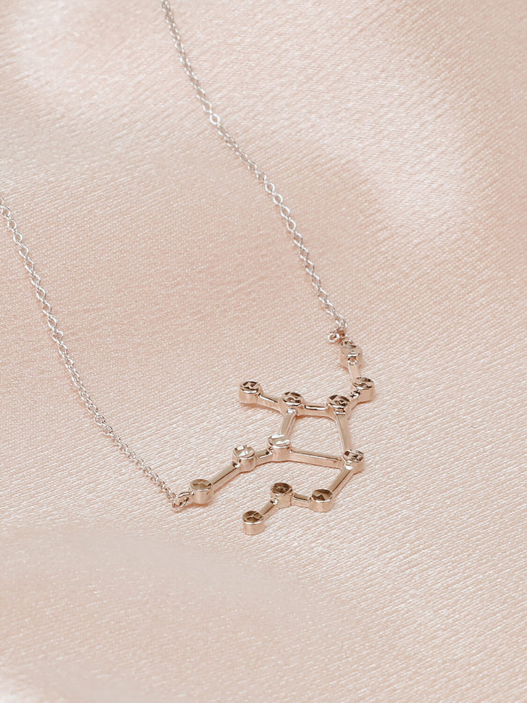 Detail photo of sterling silver Virgo zodiac constellation necklace from ModSet jewelry laying on its side on pink fabric