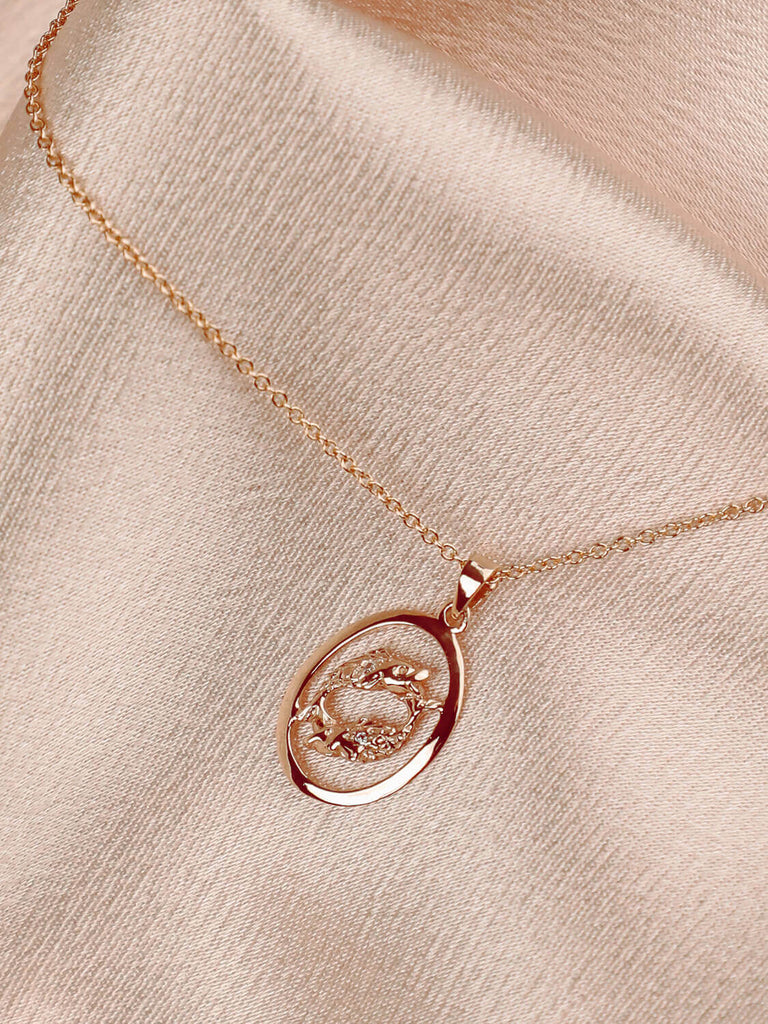 detail photo of pisces charm necklace in 14k yellow gold with diamonds against pink satin
