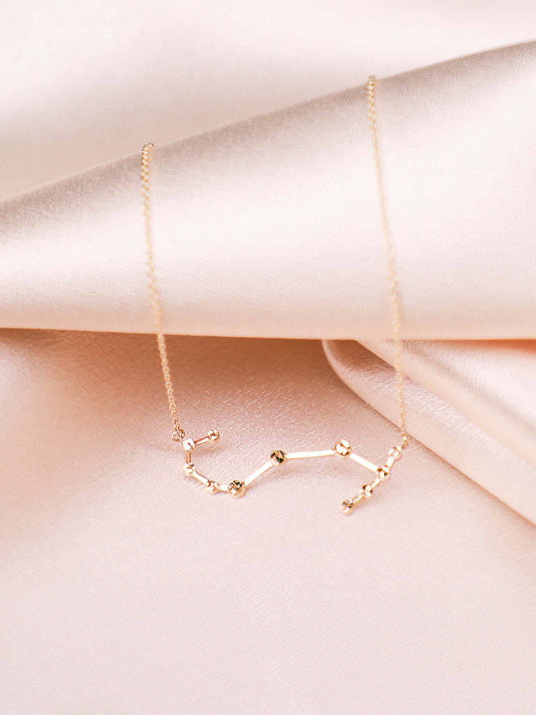 close up of gold scorpio constellation necklace on satin background