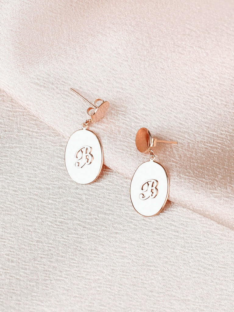 close up of pair of "B" Script initial post earrings in yellow gold on pink satin